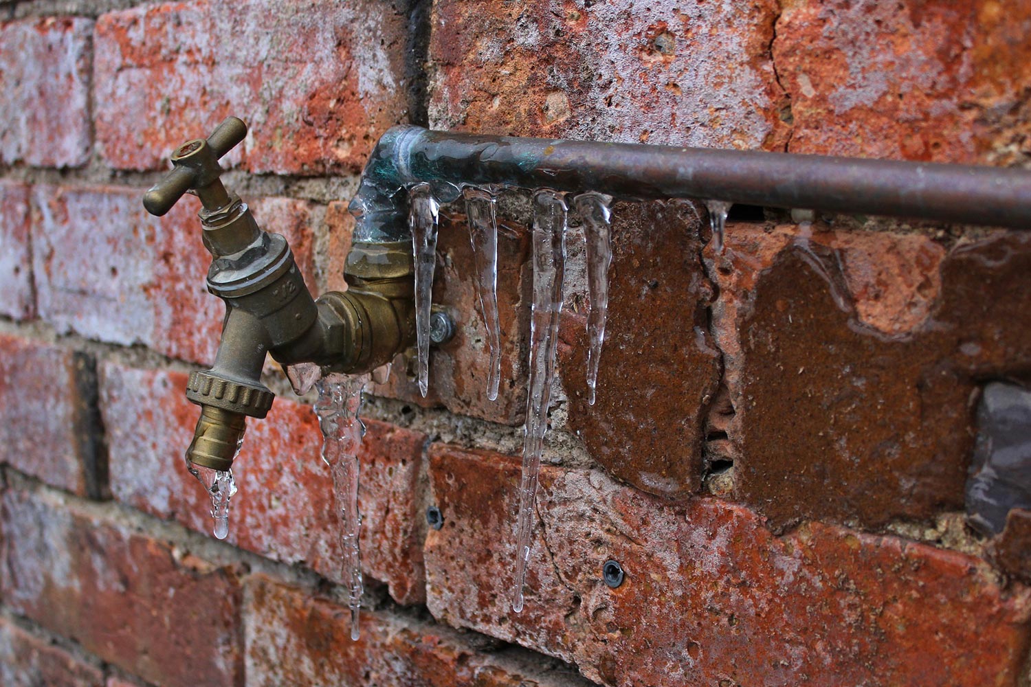 A frozen pipe outside of a brick house