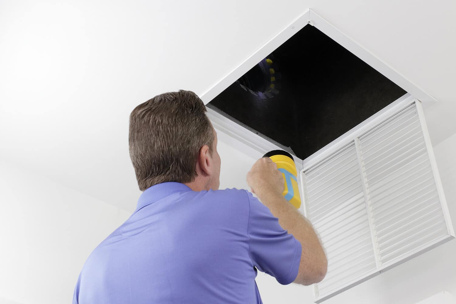 Man Inspecting an Air Duct with a Flashlight