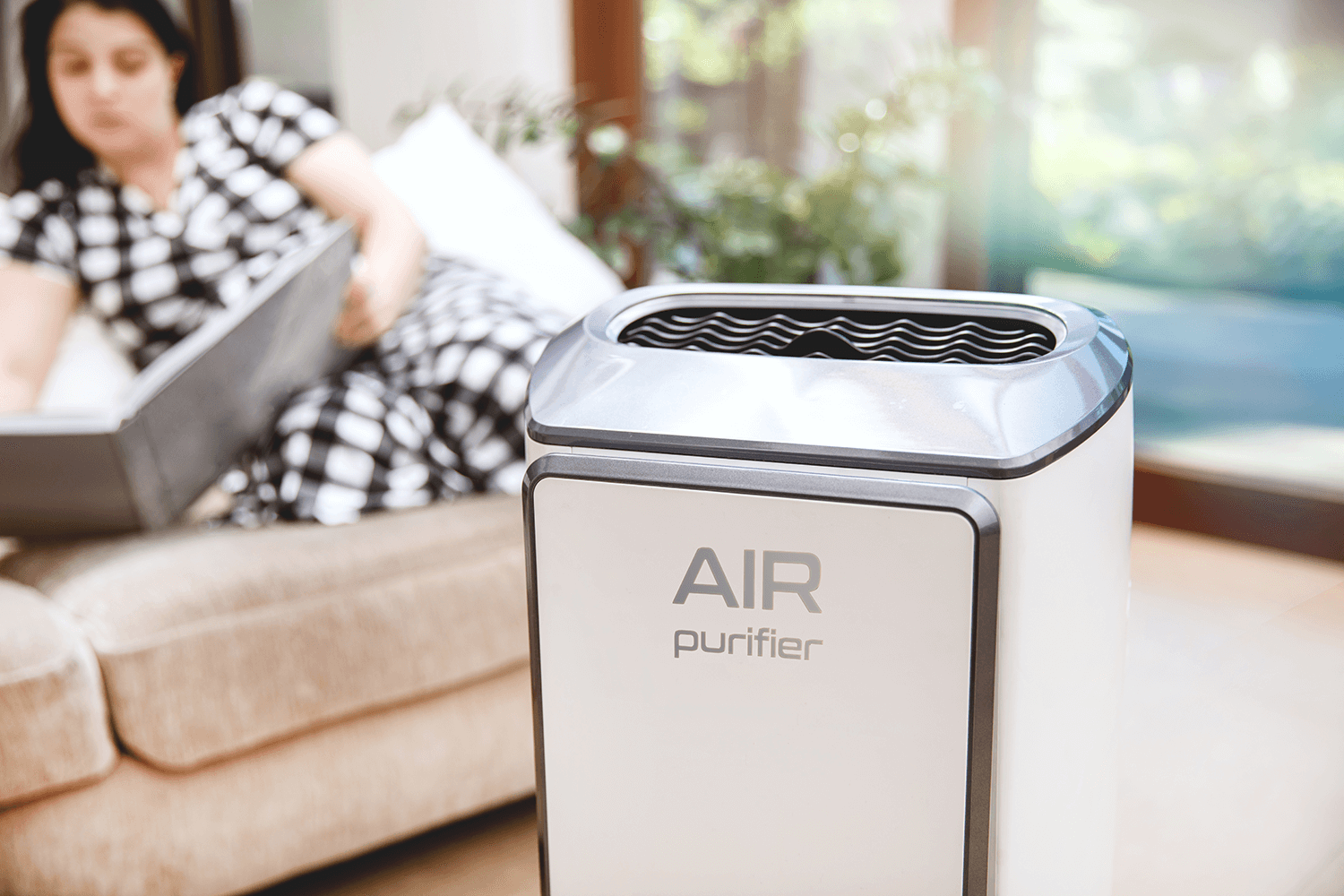 Air purifier cleans up air quality. Modern air purifier cleans up the air in the living room with woman reading a book on couch in the background.