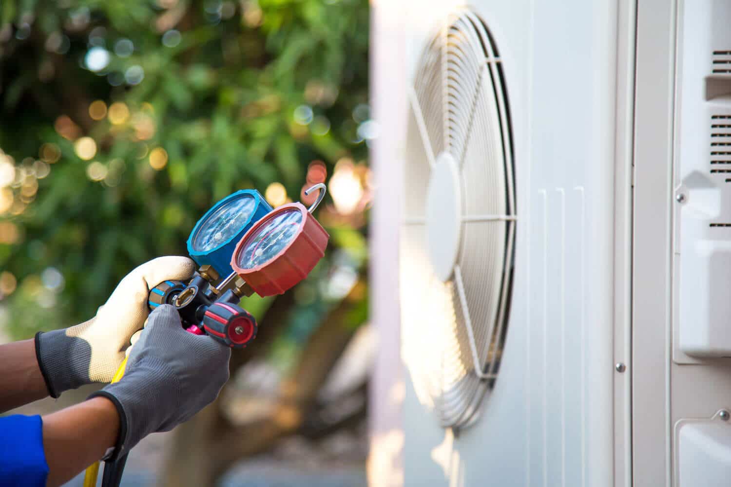 man inspecting air conditioner unit outside with gauge